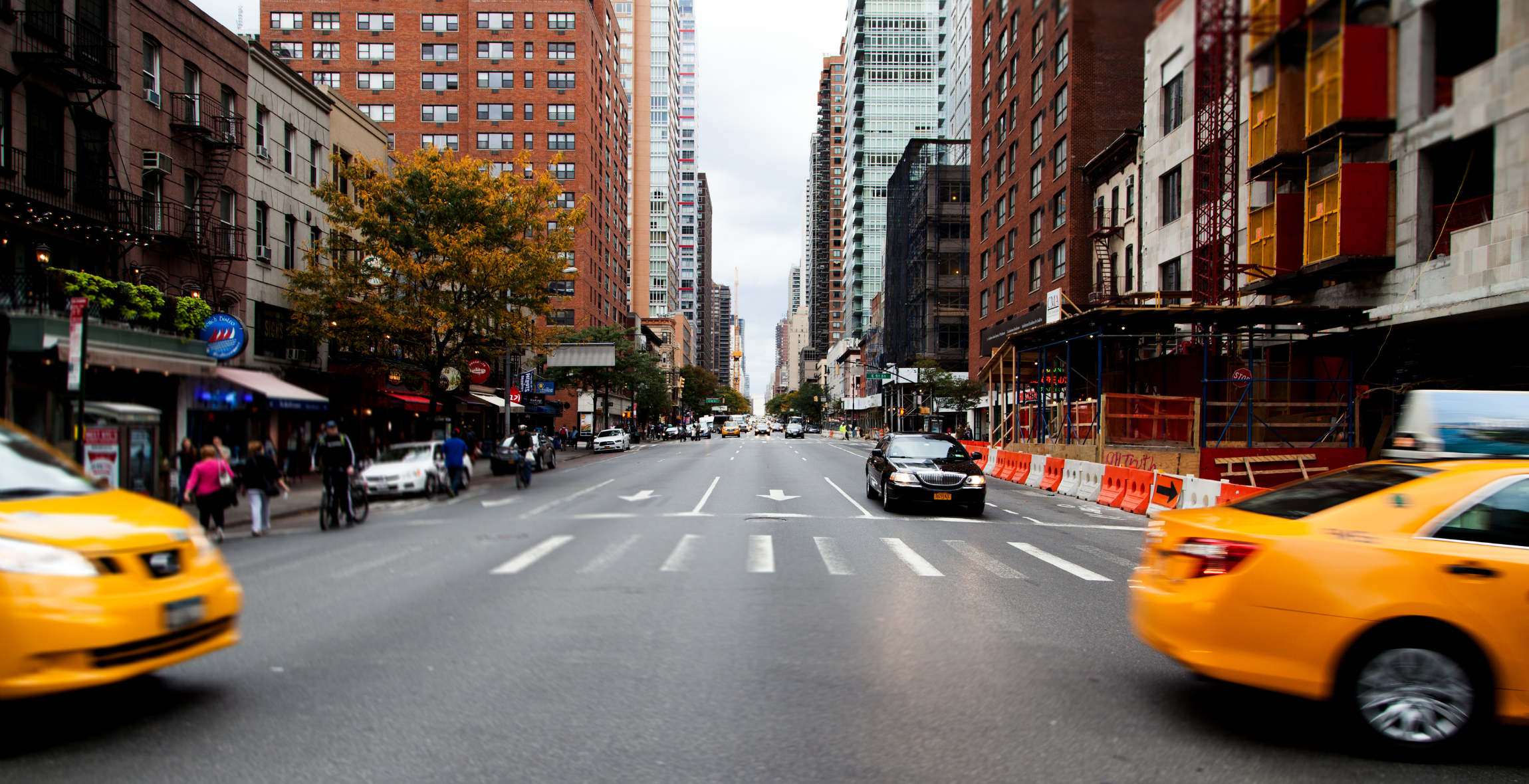 Taxis follow each other across a street surrounded by buildings in New York City.