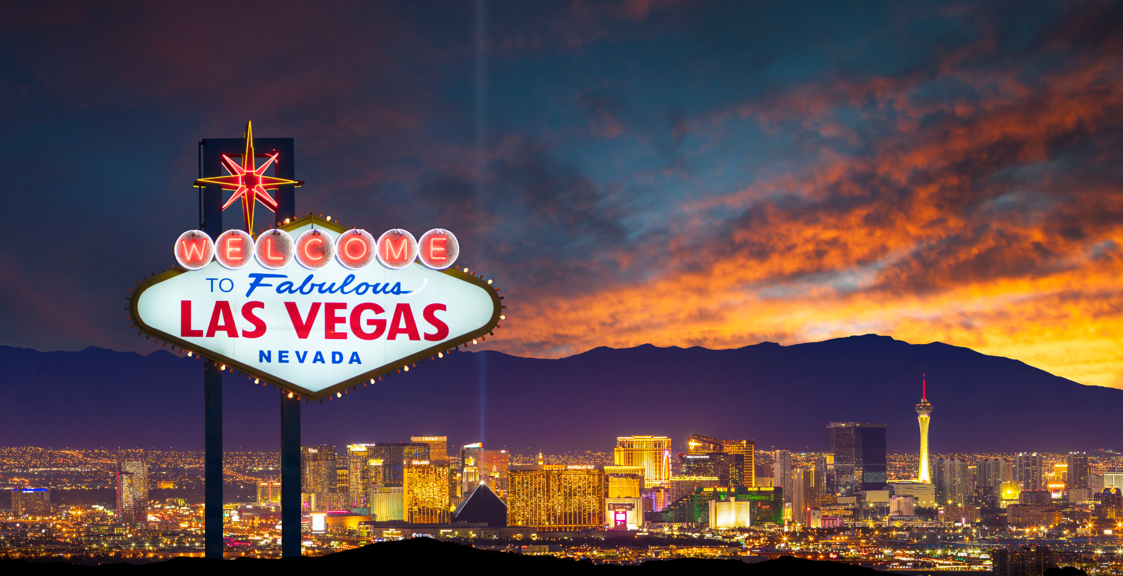 'Welcome to Fabulous Nevada' Sign is in front of a sunset and mountain and city.