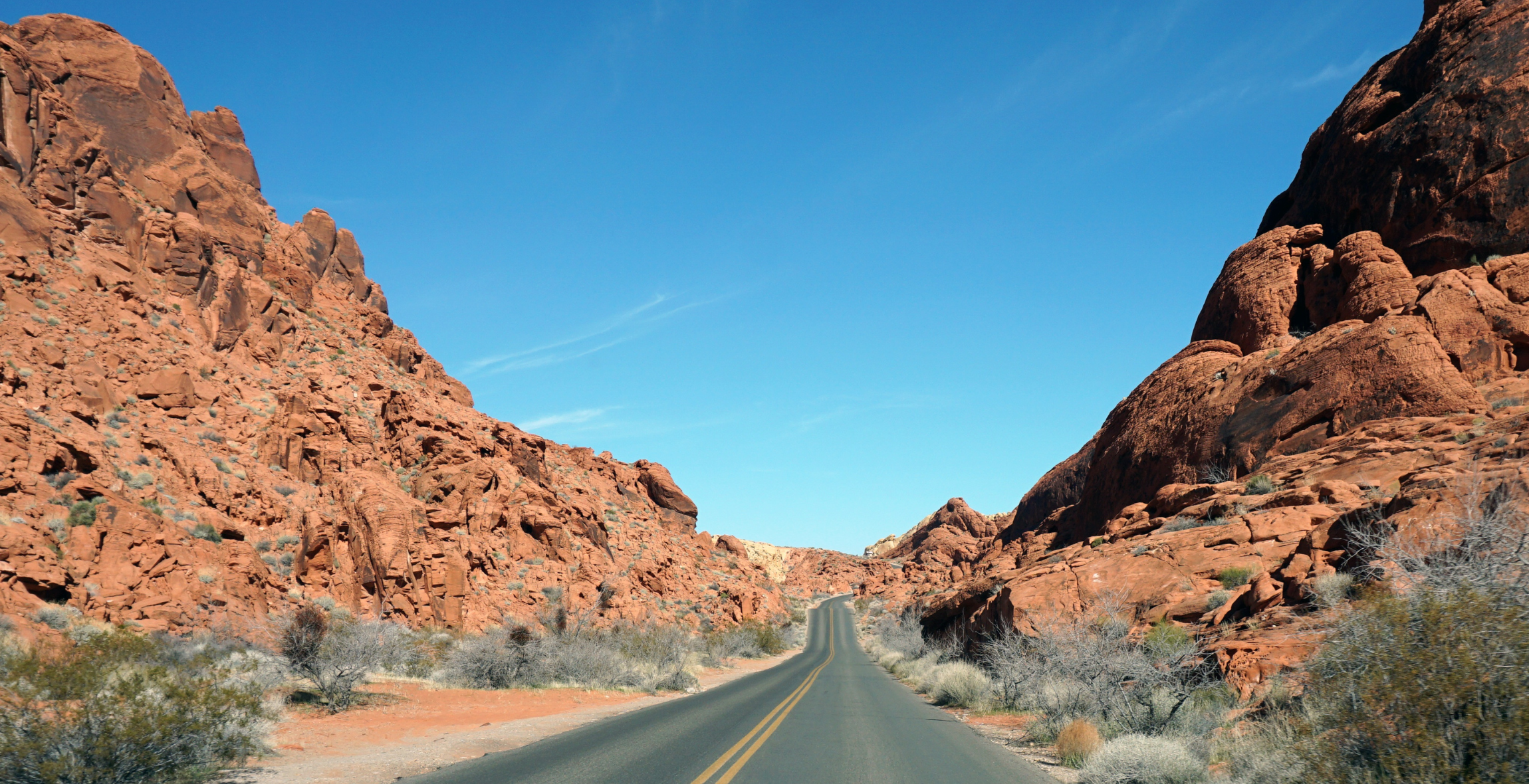 an empty road is surrounded by orange dusty rocks and mountains.